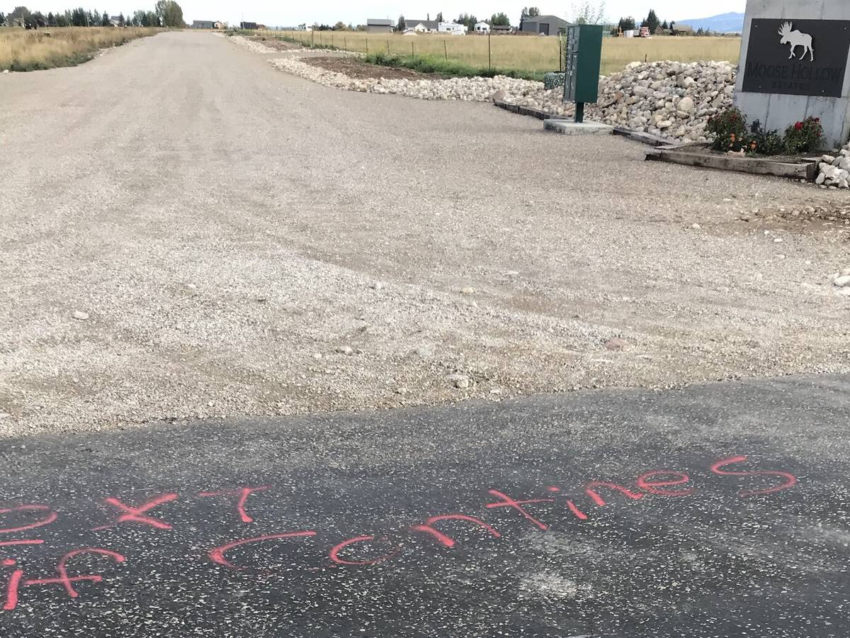 "Next if contines" spray-painted in red on the asphalt apron of a gravel road, with the Moose Hollow Estates sign at right.