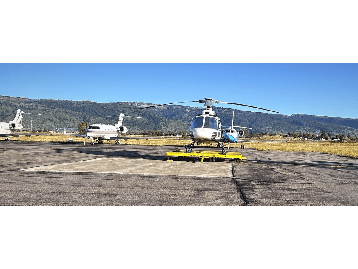Business jets and a helicopter parked on the apron at Driggs-Reed Memorial Airport, below forested foothills