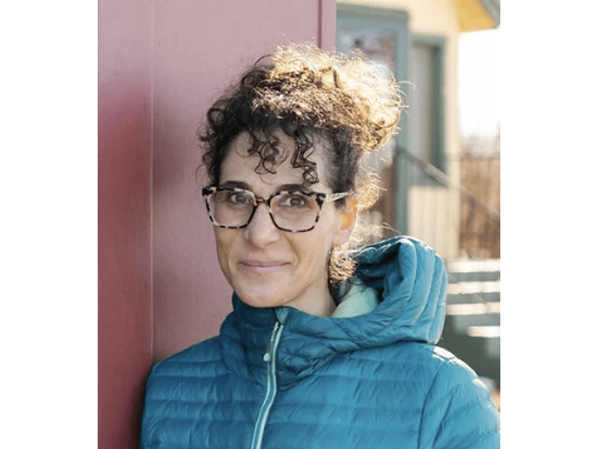 Erica Linnell, with curly dark hair and tortoiseshell glasses, in a teal puffer jacket