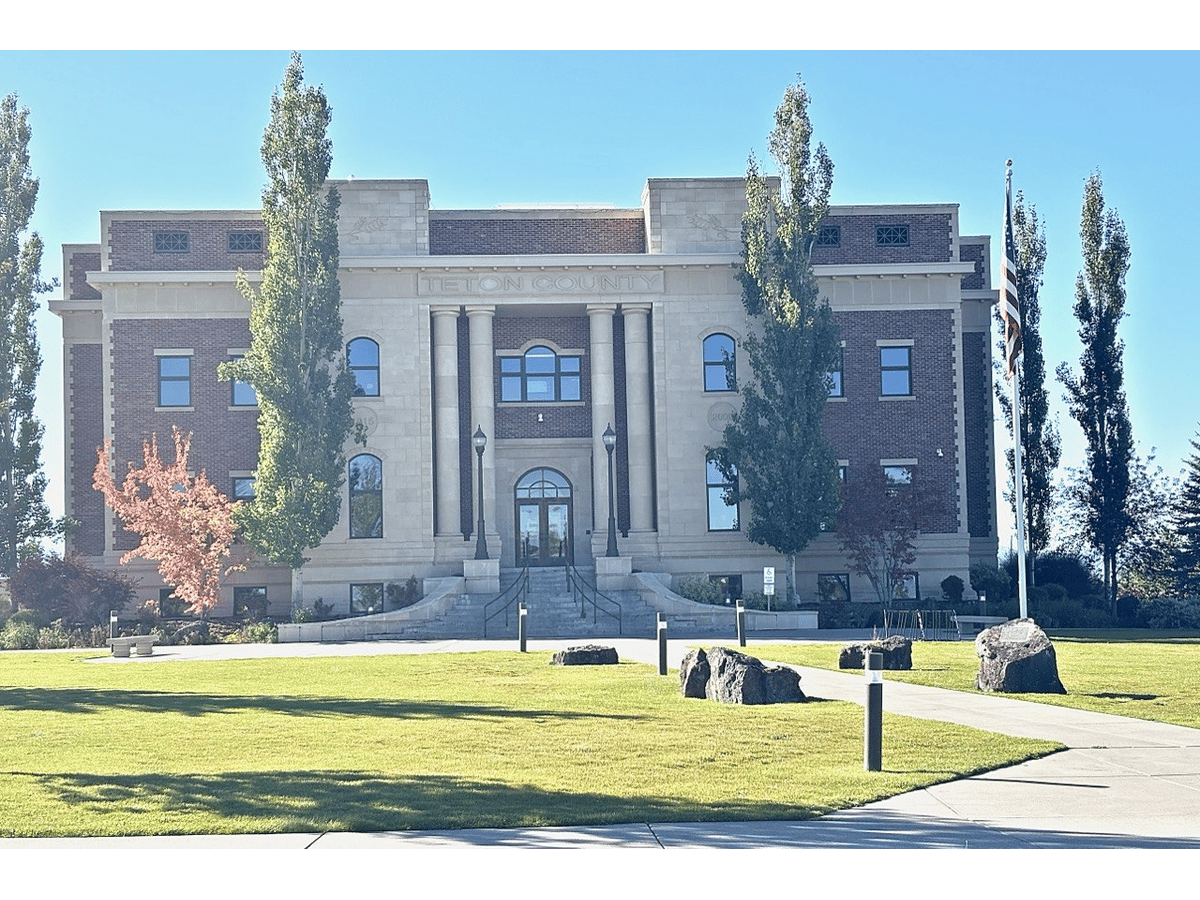 Teton County Courthouse, a columned brick-and-stone building with a lawn and young trees, on a sunny day