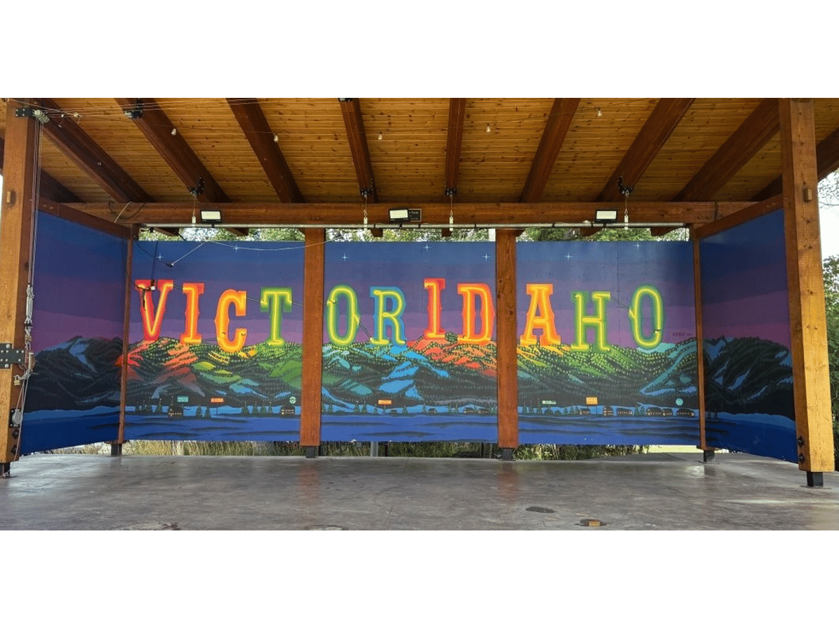 Covered outdoor stage with a colorful mural spelling "Victor Idaho" in neon letters over mountains