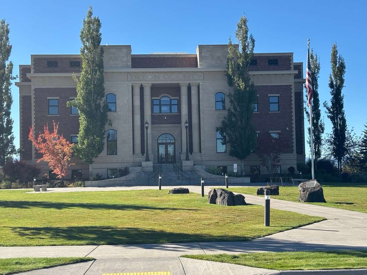 Teton County Courthouse, a columned brick-and-stone building, with a lawn and boulders out front on a clear day