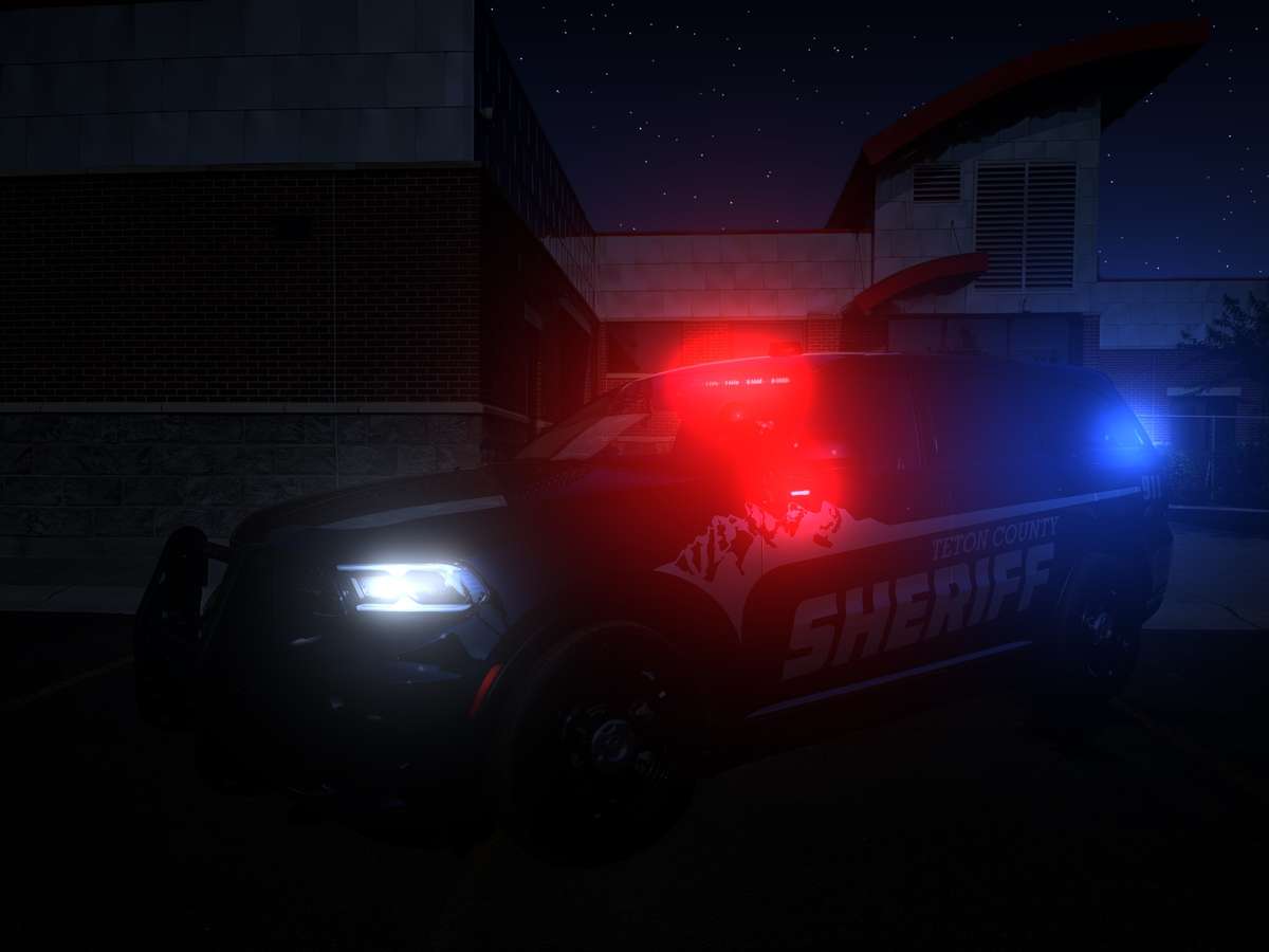 Teton County Sheriff patrol SUV at night with red and blue emergency lights flashing outside a building