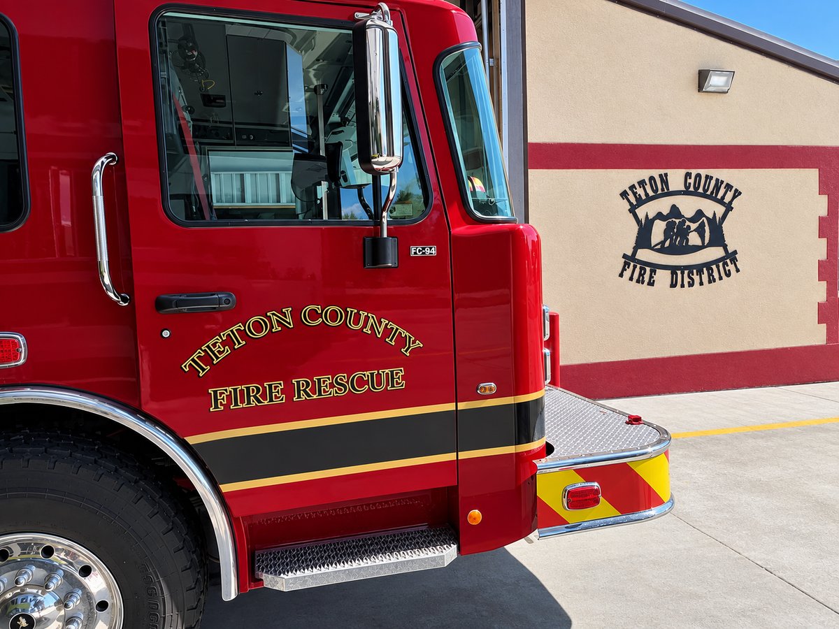 Red Teton County Fire Rescue engine parked beside a station wall bearing the Teton County Fire District emblem