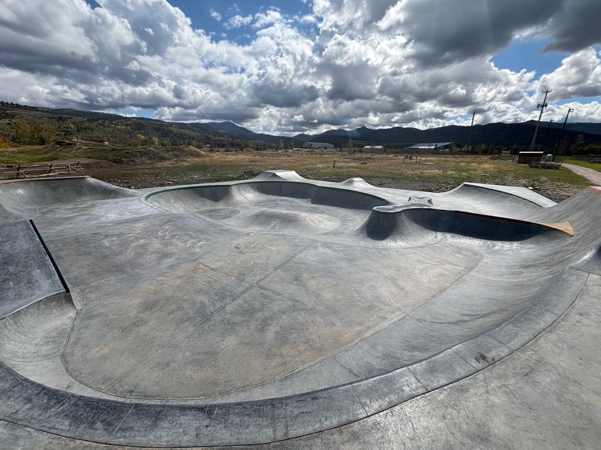 Empty concrete skate park bowls in an open field under cloudy skies with mountains in the distance